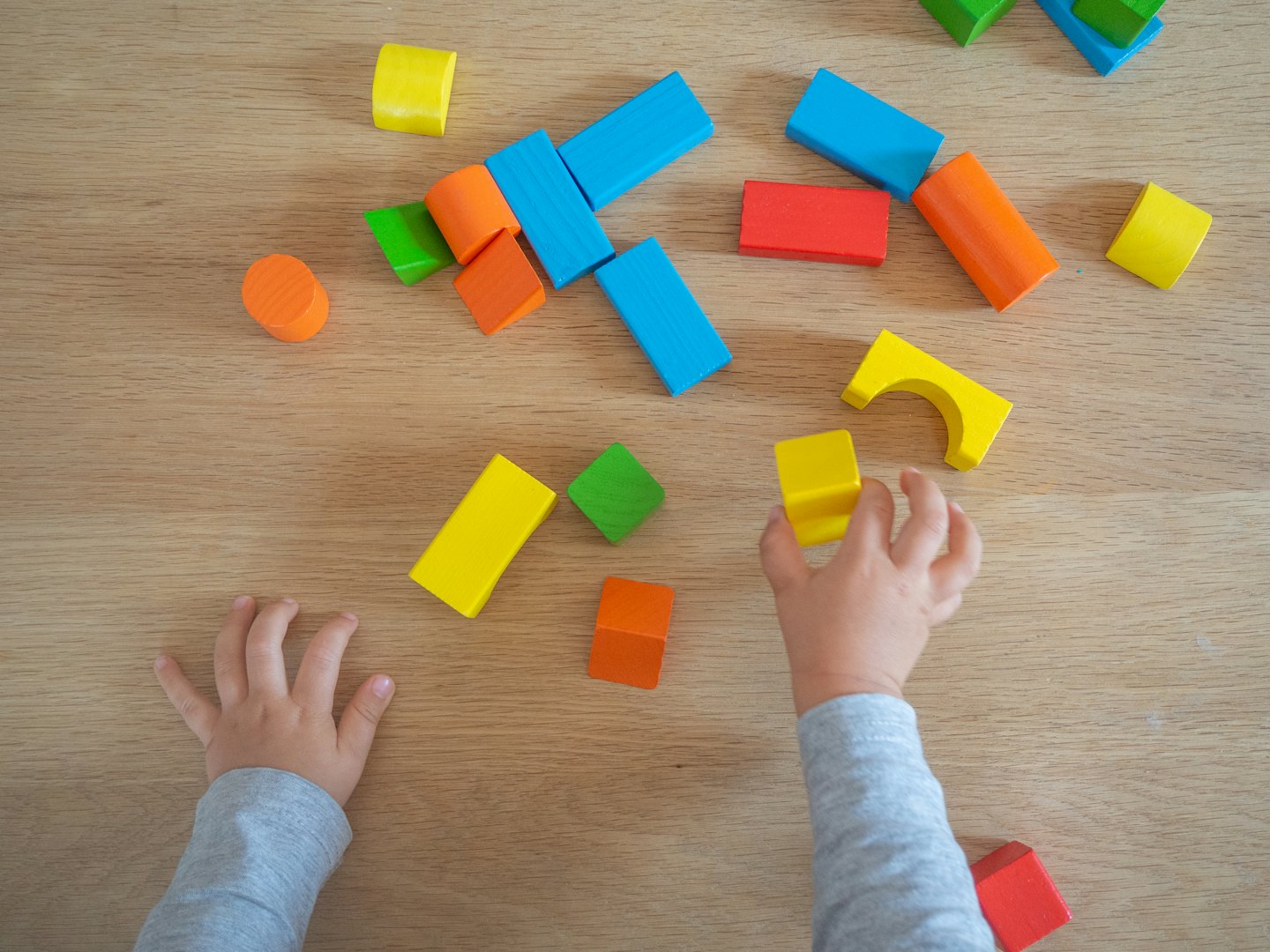 Child's hands playing with colorful wooden building blocks on a table.