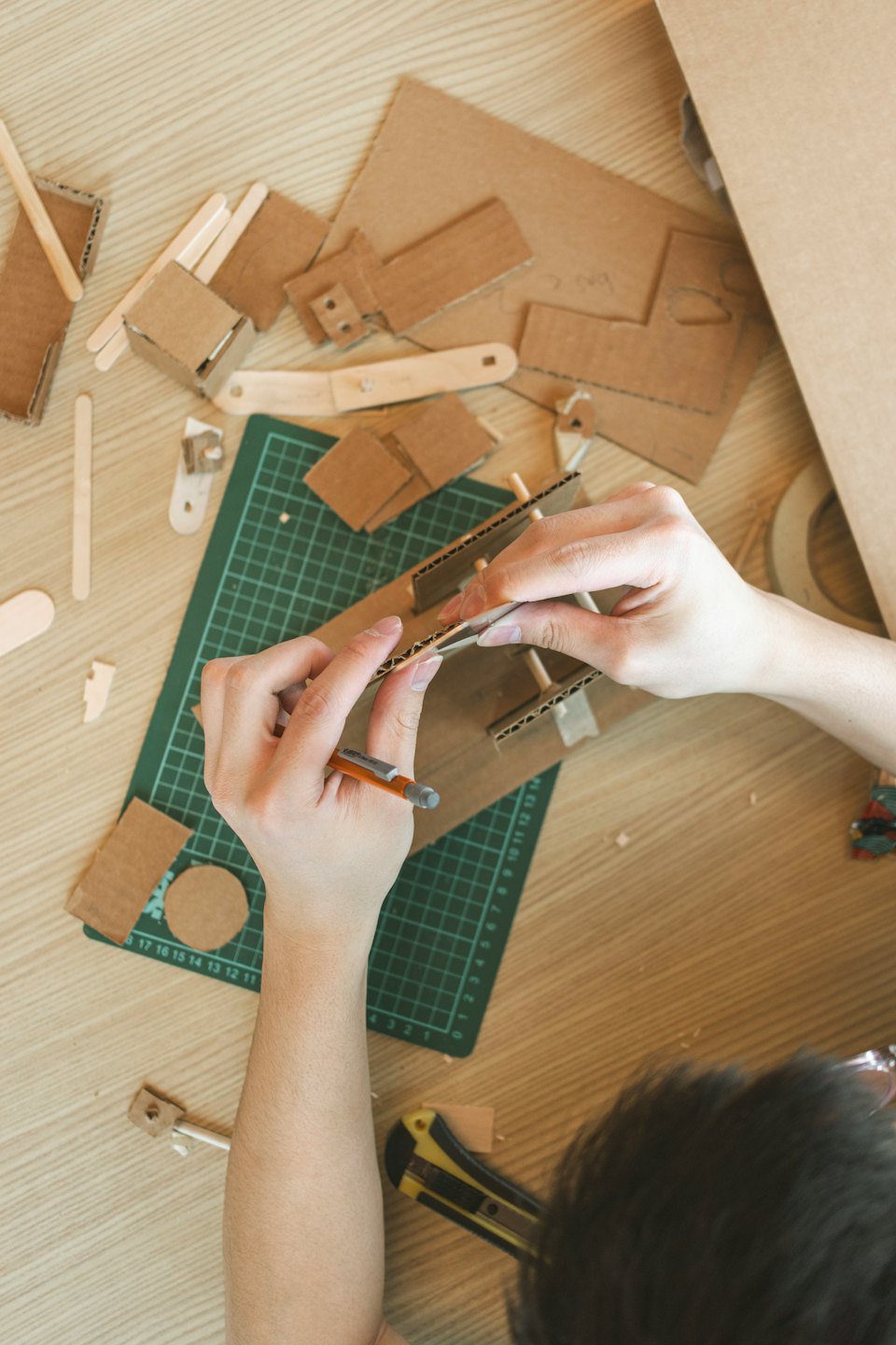 Hands assembling a cardboard craft model on a wooden table.
